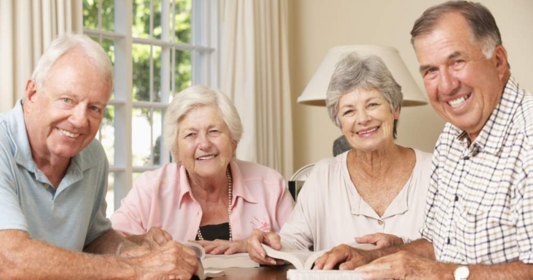 4 seniors sitting together at a table all looking straight at the viewer and smiling.